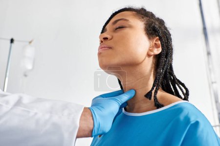 Téléchargez les photos : Malade jolie africaine américaine femme fermer les yeux tandis que son médecin indien examiner ses ganglions lymphatiques - en image libre de droit