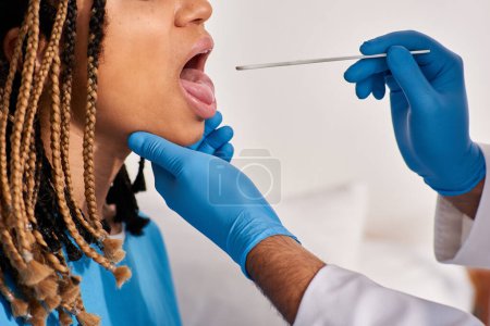 Foto de Vista recortada del médico revisando la garganta de su joven paciente afroamericano, salud - Imagen libre de derechos