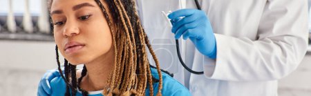 Foto de Médico indio escuchando el aliento de su paciente afroamericano enfermo con estetoscopio, pancarta - Imagen libre de derechos