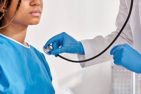 Foto de Médico indio escuchando el aliento de su paciente afroamericano enfermo con estetoscopio, recortado - Imagen libre de derechos