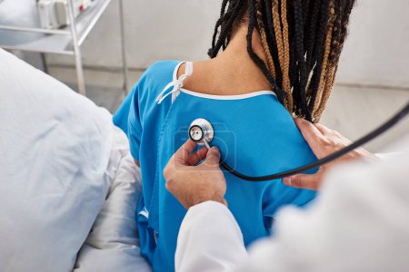 Téléchargez les photos : Vue arrière du médecin indien vérifiant le souffle de son patient afro-américain à l'hôpital - en image libre de droit