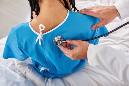 Téléchargez les photos : Vue arrière du médecin indien vérifiant le souffle de son patient afro-américain à l'hôpital - en image libre de droit