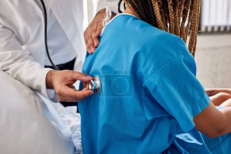 Téléchargez les photos : Jeune médecin indien examinant le souffle de son patient afro-américain avec stéthoscope, soins de santé - en image libre de droit