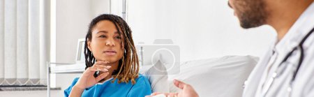 Téléchargez les photos : Afro-américaine dans un lit d'hôpital en regardant son médecin indien prendre des notes sur tablette, bannière - en image libre de droit