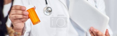 Téléchargez les photos : Vue recadrée du médecin indien avec comprimé montrant des pilules à son patient afro-américain, bannière - en image libre de droit