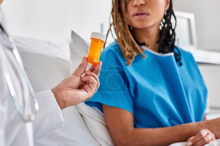 Téléchargez les photos : Femme afro-américaine malade regardant son médecin indien lui donner des pilules dans sa salle d'hôpital - en image libre de droit