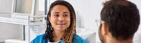 Téléchargez les photos : Focus sur jeune femme afro-américaine joyeux regardant son médecin indien flou en salle, bannière - en image libre de droit
