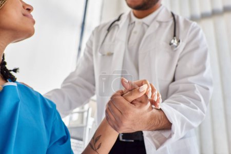Téléchargez les photos : Vue recadrée du médecin indien joyeux réconfortant son patient afro-américain dans son service hospitalier - en image libre de droit