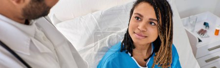 Téléchargez les photos : Se concentrer sur la femme afro-américaine joyeuse au lit en regardant calmement son médecin indien flou, bannière - en image libre de droit