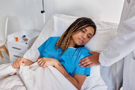 Téléchargez les photos : Vue recadrée du médecin indien réconfortant sa patiente afro-américaine malade triste, soins de santé - en image libre de droit
