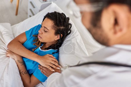 Téléchargez les photos : Vue recadrée du médecin indien réconfortant sa patiente afro-américaine malade triste, soins de santé - en image libre de droit