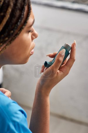 young ill african american female patient using her asthma inhaler in hospital ward, healthcare