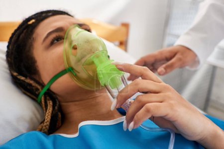 Téléchargez les photos : Vue recadrée du médecin réconfortant femme afro-américaine malade couché dans le lit d'hôpital avec masque à oxygène - en image libre de droit