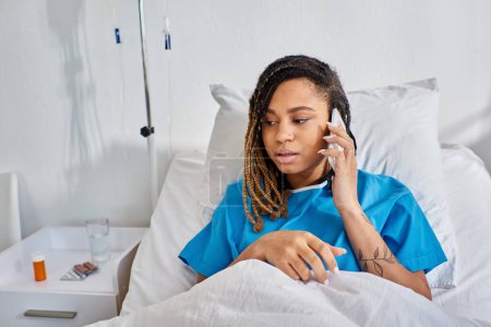 joven afroamericana enfocada hablando por teléfono y sonriendo en su sala de hospital, atención médica