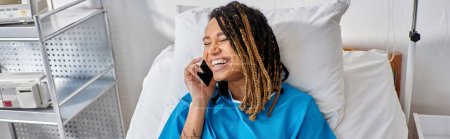Téléchargez les photos : Jeune femme afro-américaine joyeux parlant par téléphone et souriant dans sa salle d'hôpital, soins de santé - en image libre de droit