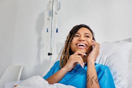 fröhliche junge afrikanisch-amerikanische Frau telefoniert und lächelt auf ihrer Krankenstation, Gesundheitswesen