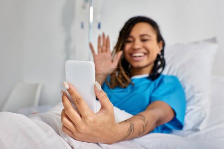 attractive young african american woman having video call while lying in hospital bed, healthcare