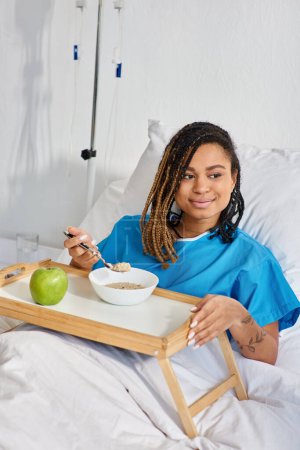 afrikanisch-amerikanische Frau mit Brei und Apfel zum Frühstück auf ihrer Krankenstation, Gesundheitswesen