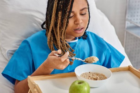 afrikanisch-amerikanische Frau mit Brei und Apfel zum Frühstück auf ihrer Krankenstation, Gesundheitswesen