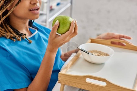 abgeschnittene Ansicht einer jungen afrikanisch-amerikanischen Frau beim Frühstück im Krankenhausbett, Gesundheitswesen