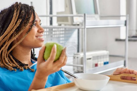 jeune femme afro-américaine ayant du porridge et de la pomme pour le petit déjeuner en salle d'hôpital, soins de santé