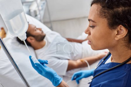 Téléchargez les photos : Focus sur afro-américain infirmière réglage drop counter à côté de son flou indien patient masculin - en image libre de droit