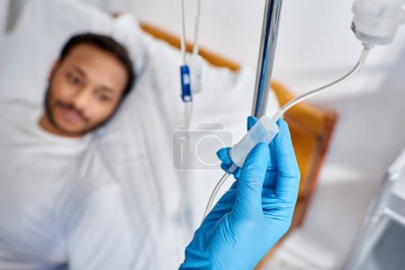 Téléchargez les photos : Focus sur le cadre infirmier afro-américain drop counter à côté de l'homme flou couché dans le lit d'hôpital - en image libre de droit