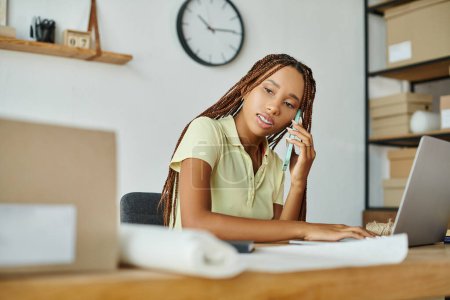 atractiva mujer afroamericana comerciante hablando por teléfono mientras trabaja en sus paquetes, entrega