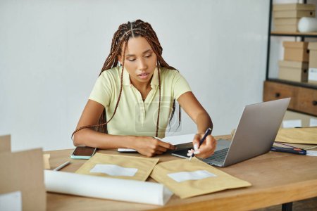atractiva mujer afroamericana comerciante tomando notas mientras trabaja duro, concepto de entrega
