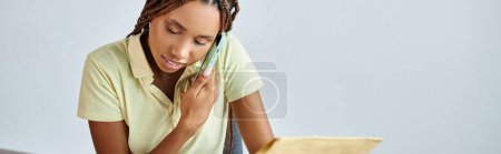 beautiful african american seller holding post packet and talking by phone, delivery concept, banner