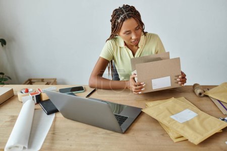Foto de Atractivo joven afroamericano mujer vendedor embalaje caja de cartón cuidadosamente, concepto de entrega - Imagen libre de derechos