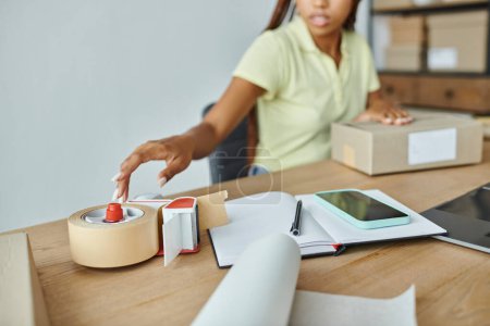 cropped view of young african american female seller using tape to pack cardboard box, delivery