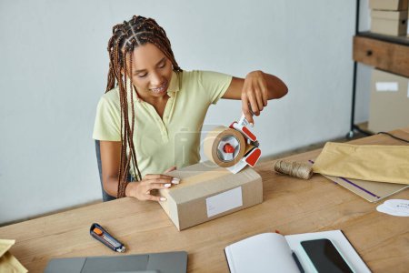 Foto de Alegre joven afroamericano minorista femenino utilizando cinta en caja de cartón, concepto de entrega - Imagen libre de derechos