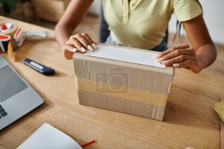 cropped view of young african american female seller packing cardboard box, delivery concept