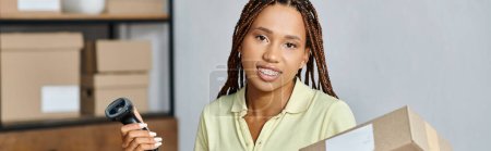 Foto de Mujer femenina afroamericana bonita sonriendo a la cámara mientras trabaja duro, concepto de entrega, pancarta - Imagen libre de derechos