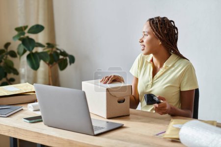 attractive african american woman holding scanner and looking away next to box while working hard