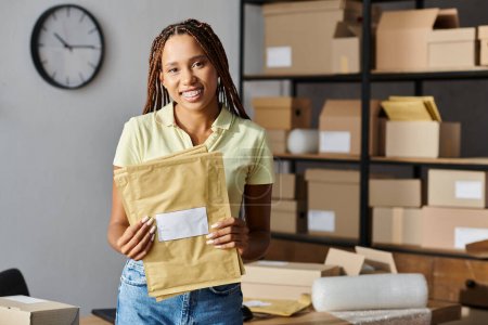 cheerful young african american female merchant holding post packets and smiling at camera, delivery