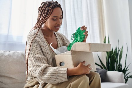 joyous attractive african american woman with braces in homewear looking at her new green shoes