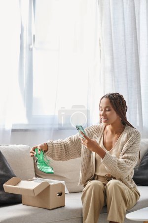 Téléchargez les photos : Joyeuse femme afro-américaine attrayante avec des bretelles souriantes et prenant des photos de ses nouvelles chaussures vertes - en image libre de droit