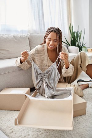 joyous attractive african american woman unpacking her new chic silver dress and smiling joyfully