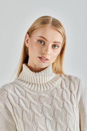 portrait of beautiful blonde woman in  white knitted sweater looking at camera on grey, winter style