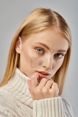 close up portrait of young blonde in winter sweater with blonde hair and natural makeup on grey