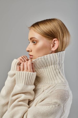 Téléchargez les photos : Portrait de profil de femme blonde en chandail tricoté blanc avec col montant sur gris, style hiver - en image libre de droit