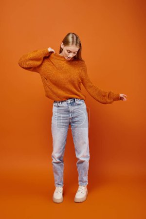 Téléchargez les photos : Jolie femme blonde en chandail tricoté lumineux et jeans sur fond orange, style hiver - en image libre de droit