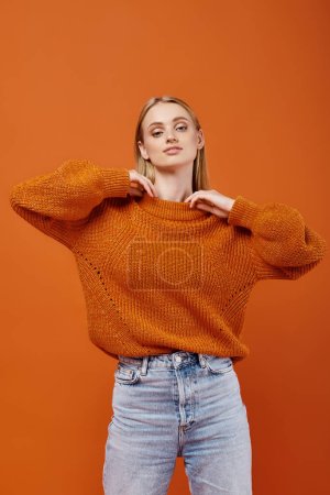 Téléchargez les photos : Femme blonde élégante en pull tricoté chaud et lumineux et un jean bleu sur fond orange, la mode - en image libre de droit
