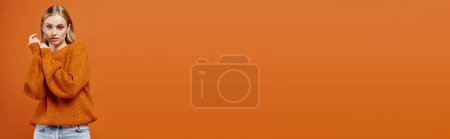 Téléchargez les photos : Femme blonde à la mode en pull tricoté confortable regardant la caméra sur fond orange, bannière - en image libre de droit