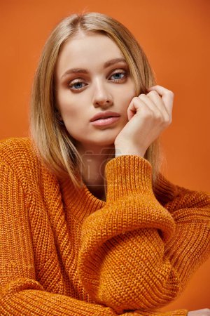 Porträt einer jungen Frau in buntem Strickpullover mit blonden Haaren und natürlichem Make-up auf orange