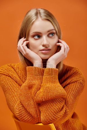 dreamy blonde woman in bright and soft knitted sweater with natural makeup looking away on orange