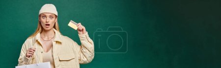 Photo for Surprised woman in stylish winter clothing with shopping bag and credit card on green, banner - Royalty Free Image