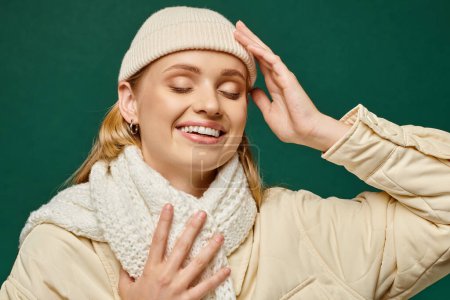 Téléchargez les photos : Femme joyeuse en veste d'hiver et écharpe tricotée avec bonnet chapeau souriant avec les yeux fermés sur le vert - en image libre de droit